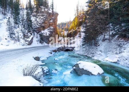 Der Fluss eines schönen blauen Flusses in der Nähe einer Bergstraße in Kiefernwald. Winterlandschaft. Stockfoto