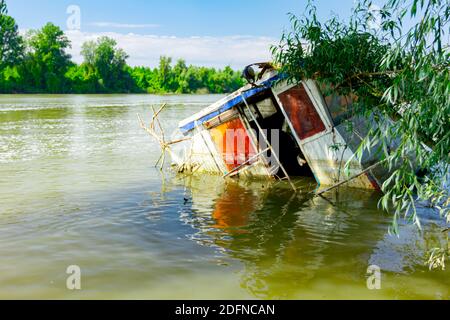 Wracked kleines Fischerboot ist teilweise überflutet, steht an der Küste des breiten Flusses. Stockfoto