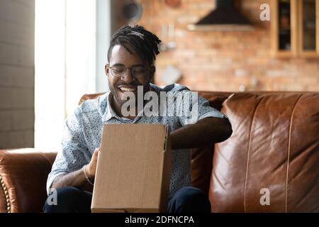 Lächelnder junger afroamerikanischer Mann beim Auspacken des Pakets. Stockfoto
