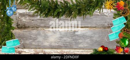 Weihnachten während der COVID 19 Pandemiekonzept. Oben sehen Doppelrand mit Dekorationen, Gesichtsmasken und Handdesinfektionsmittel über einem Holzhintergrund. Stockfoto