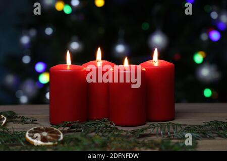 Eine Nahaufnahme brennender roter Adventskerzen auf einer Holzfläche, vor bunten Bokeh-Lichtern Stockfoto