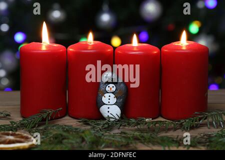 Eine Nahaufnahme brennender roter Adventskerzen auf einer Holzfläche, vor bunten Bokeh-Lichtern Stockfoto