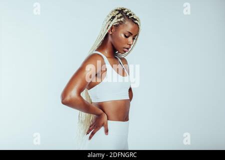 Seitenansicht Nahaufnahme der afroamerikanischen athletischen Frau auf weißem Hintergrund. Portrait von Fitness-Frau mit geflochtenen Haaren stehend mit Händen auf der Taille. Stockfoto