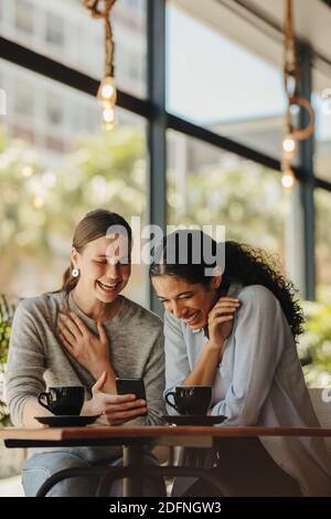 Freunde treffen sich im Café und schauen auf Handy. Frau, die ihrem Freund das Telefon zeigt und lächelt. Stockfoto
