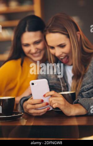 Freundinnen treffen sich im Café und schauen auf Handy. Frau zeigt etwas Lustiges auf ihrem Handy an Freund. Stockfoto