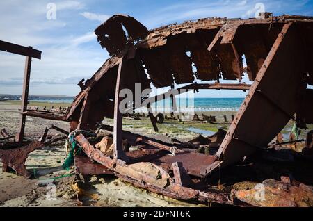 Altes verlassene rostige Boot liegt am Strand. Total beschädigte Metallschiff an der Meeresküste in der Nähe von Hafen in Puerto Madryn, Chubut, Argentinien Stockfoto