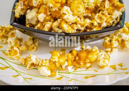 Nahaufnahme von süßem und Crunchy Caramel Popcorn in einer Schüssel Und verschüttet auf eine Platte darunter Stockfoto