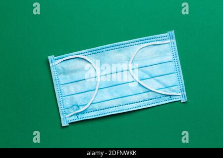 OP-Maske mit Gummi-Ohrbändern auf grünem Hintergrund. Typische 3-lagige OP-Maske, um Mund und Nase zu bedecken. Prozedur Maske von Bakterien. Oben Stockfoto