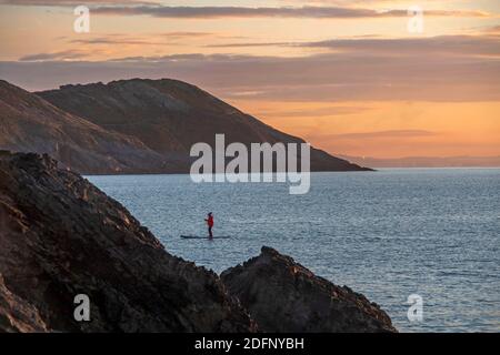 Swansea, Großbritannien. Dezember 2020. Paddelboarder kurz nach Sonnenaufgang auf dem ruhigen Meer vor Snaple Point in Langland Bay in der Nähe von Swansea an einem kalten und frostigen Morgen, als die Temperatur kämpfte, um über Null Grad zu bekommen. Quelle: Phil Rees/Alamy Live News Stockfoto