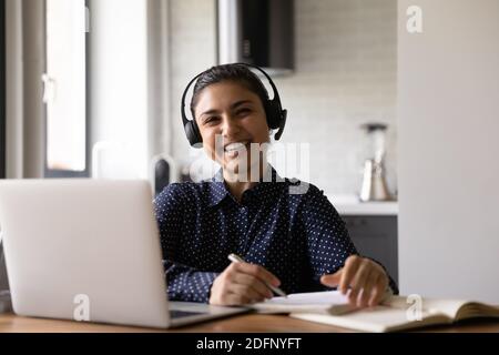 Fröhliche tausendjährige hindu-Frau, die von zu Hause aus mit Laptop-Ohrhörern studiert Stockfoto