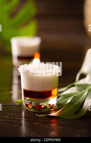 Tropische alkoholische Aufnahmen mit Kokosflocken, Monstera Blume mit Kokosnuss und Ananas auf braunem Holzhintergrund dekoriert Stockfoto