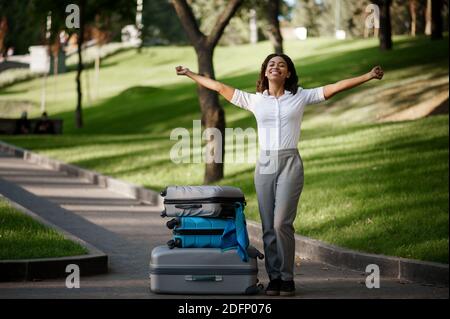 Fröhliche Frau mit Koffer zu Fuß im Park Stockfoto