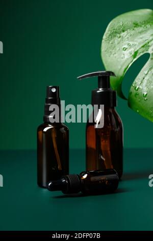 Amber Glas Kosmetikflaschen Set und Monstera Blatt auf grünem Hintergrund. Natürliche Bio-Beauty-Produkte Verpackung ohne Etiketten. Stockfoto