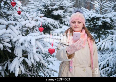 Glückliche nette Frau macht Selfie Foto am Telefon im Winterwald in der Nähe von weihnachtsbaum - Moskau, Russland, 02. Dezember 2020 Stockfoto