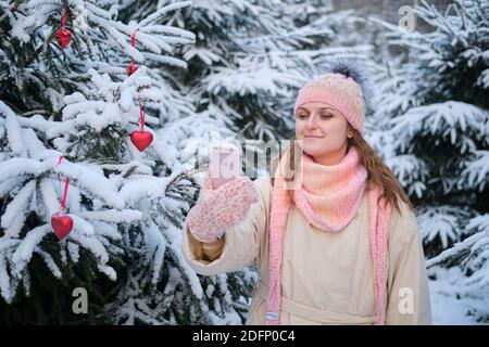 Nette Frau mit dem Telefon steht allein im Winterwald in der Nähe des Weihnachtsbaums - Moskau, Russland, 02. Dezember 2020 Stockfoto