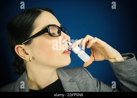 Junge Frau in Brille, verwendet Nasenspray auf blauem Hintergrund. Stockfoto