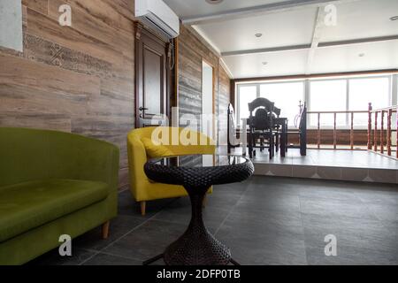 Designermöbel mit einem grünen Sofa, einem Sofa und einem gelben Sessel, einem Stuhl neben einem Rattantisch mit einem Arbeitsbereich aus Feinsteinzeug. Stockfoto