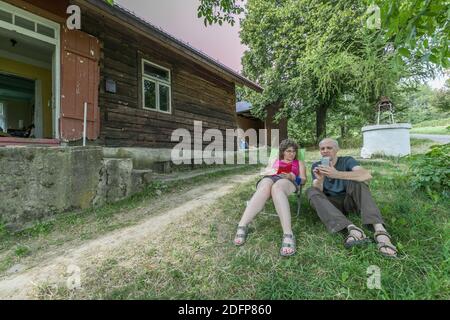 Teodorówka, Polen - 18. August 2017: Das Paar sitzt vor dem Holzhaus und schaut in das Mobiltelefon. Osteuropa. Stockfoto