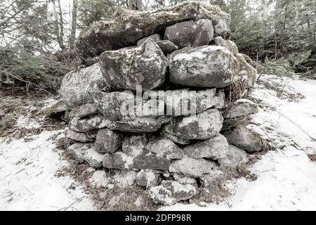 Ein alter, rauer Steinhaufen auf der Seite eines Hügels. Sehr niedrige Sättigung, fast schwarz und weiß. Die Steine sind schmutzig und mit Moos und Flechten bedeckt. Stockfoto