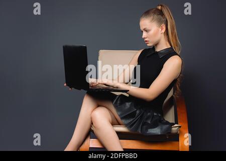 Seriöse Geschäftsfrau mit Laptop im Sessel auf grauem Hintergrund mit leerem Seitenraum. Online-Konferenz Stockfoto