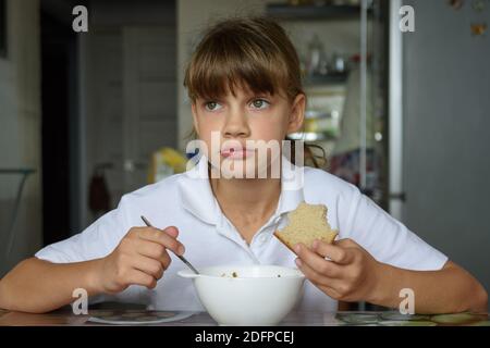 Mädchen isst nachdenklich Suppe am Tisch in der Küche Stockfoto