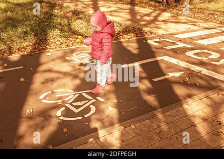 Ein kleines Mädchen geht entlang eines Radweges im Park. Herbst. Stockfoto