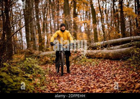 Schöner junger Mann, der beim Radfahren durch den Herbst eine Bremse zieht Wald Stockfoto