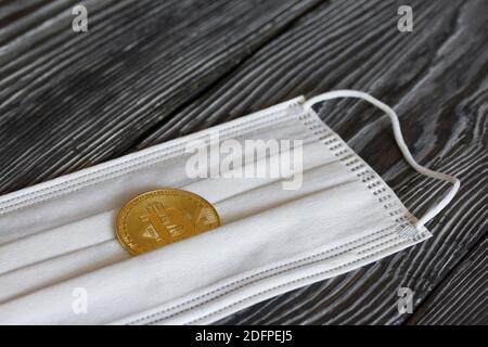 Bitcoin liegt auf einer medizinischen Maske. Auf Kiefernbrettern. Stockfoto