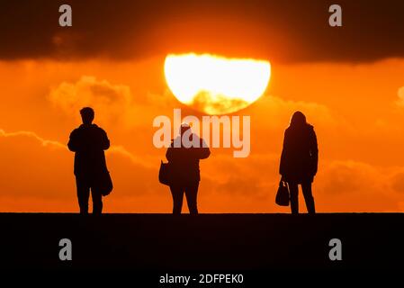 Lyme Regis, Dorset, Großbritannien. Dezember 2020. Wetter in Großbritannien. Die Leute, die am späten Nachmittag spazieren gehen, werden gegen den Sonnenuntergang auf der Cobb Harbour Wall bei Lyme Regis in Dorset am Ende eines kalten Tages mit sonnigen Zaubersprüchen silhouettiert. Bild: Graham Hunt/Alamy Live News Stockfoto