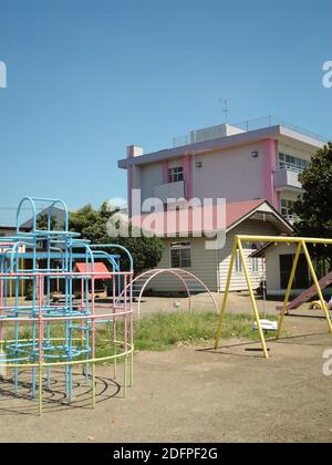 Ein traditioneller japanischer Grundschule Spielplatz mit Rutsche, Schaukel und Reifen mit Gebäuden im Hintergrund im ländlichen Japan Stockfoto