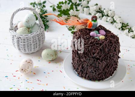 Osterschokolade Kuchen und Vogel im Nest sitzen. Kleiner orangefarbener Vogel, bunte Eier und Weidenkorb auf einem Hintergrund des Osterdekors Stockfoto