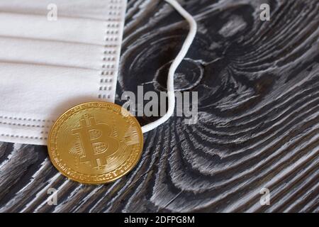 Bitcoin liegt auf einer medizinischen Maske. Auf Kiefernbrettern. Stockfoto