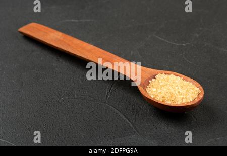 Holzlöffel mit braunem Zucker auf dunklem Grund Stockfoto