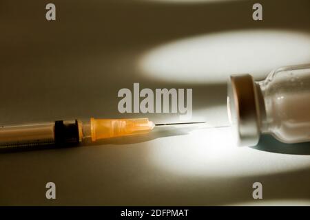 Orangefarbene Kanülenspritze mit durchsichtigem Glas-Impfstofffläschchen (mit Platz für Text), heller Hintergrund Stockfoto