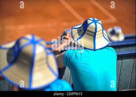 Der Mann trägt einen Strohsonnenhut und beobachtet ein Tennisspiel an einem sonnigen und heißen Sommertag. Stockfoto