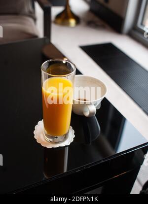 Bild mit geringer Schärfentiefe (selektiver Fokus) mit einem Glas Orangensaft in der Nähe einer fast leeren Tasse Kaffee auf einem Tisch. Stockfoto