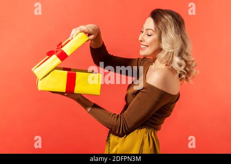 Glücklich schöne Frau Aubox großen gelben Geschenk und Blick nach innen mit zufriedenen Lächeln im Gesicht, genießen Gegenwart. Innenaufnahmen im Studio isoliert auf oder Stockfoto