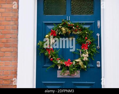 Kompostierbarer Adventskranz mit immergrünen Blättern, roten und goldenen Bändern und Zuckerrüben. Kranz hängt an einer blauen Haustür in Highgate, London. Stockfoto