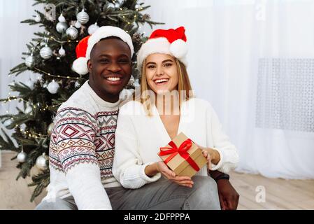 Portrait eines lächelnden jungen Paares sitzen in der Nähe von Weihnachtsbaum Feiern Sie gemeinsam das neue Jahr. Glücklicher Mann und Frau genießen Winterurlaub Feier in der Nähe decora Stockfoto