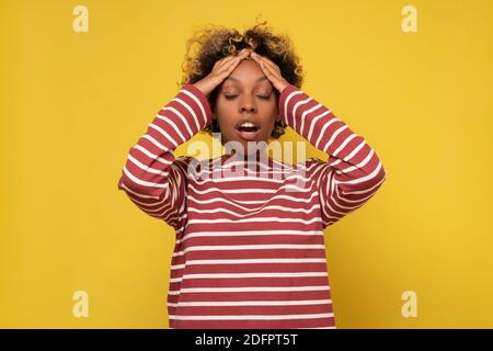 Junge afrikanische Frau, die unter schrecklichen Kopfschmerzen leidet. Studio auf gelber Wand. Stockfoto