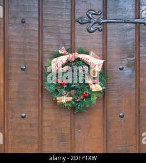 Ein hausgemachtes Weihnachtskranz auf einer Holztür mit schwarzen Armaturen. Stockfoto