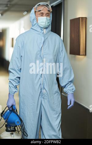 Männlicher Spezialist in Hazmat Anzug mit Desinfektionsmittel im Hotel beim Gehen im Flur. Coronavirus und Quarantänekonzept Stockfoto