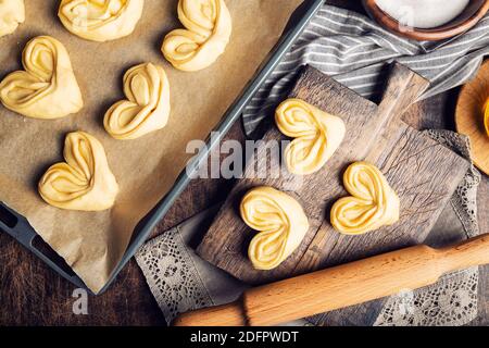 Rohe, ungebackene hausgemachte süße Brötchen mit Honig und Zucker auf rustikalem Sperrholzhintergrund. Vorbereitung zum Backen. Draufsicht. Stockfoto