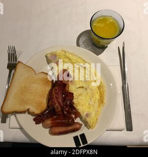 Ein Blick von oben auf hausgemachte Spiegeleier mit Würstchen, Toast und Speck auf einem Teller mit einem Glas Orangensaft Stockfoto