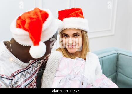 Die Frau erhielt ein Geschenk von der Geliebten. Junge schöne Frau in santa Hut sitzt auf dem Sofa lächelnd Blick auf die Kamera. Stockfoto