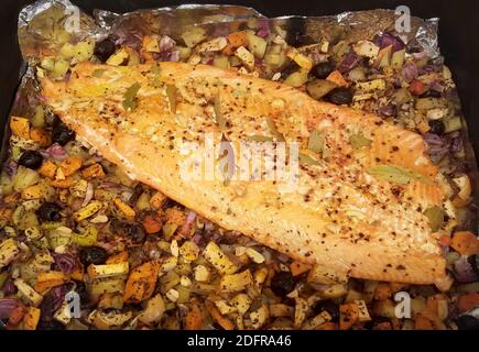 Lachsfilet gewürzt mit Pfeffer und Lorbeerblättern, im Ofen auf einer Kartoffel-Gemüse-Mischung geröstet Stockfoto
