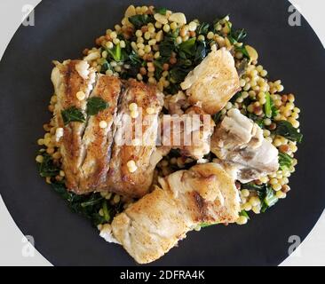 Gesunde Ernährung mit einem Teller gebackenen weißen Fisch auf einer Kichererbsen-Spinat-Mischung. Stockfoto