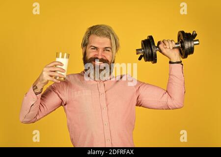 Quelle von Kalzium. Bärtiger Mann trinkt Milch. Trainieren Sie im Fitnessstudio. Milch gute Nährstoffe. Menge an Fett. Vitamine für Muskeln. Sportler halten Hantel und Glas Milch. Protein-Diät. Protein-Cocktail. Stockfoto