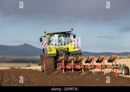 Ein Claas Axion 940 Traktor pflügt mit einem Kverneland Variomat Reversible Pflug in Schottland, mit Bennachie im Backgound Stockfoto