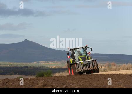 Ein Herbstblick in Richtung Bennachie in Aberdeenshire, mit einem Claas Axion 940 Traktor, der das Feld im Vordergrund pflügt Stockfoto